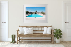 A room with 2 doors & a wooden bench. There is a picture of a swimmimg pool on the wall