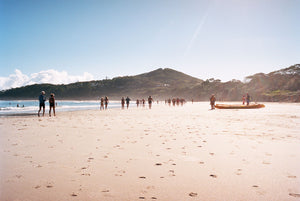 Byron bay beach with people walking in the distance, blue calm water, blue sky. Two men on a kayak head to the water