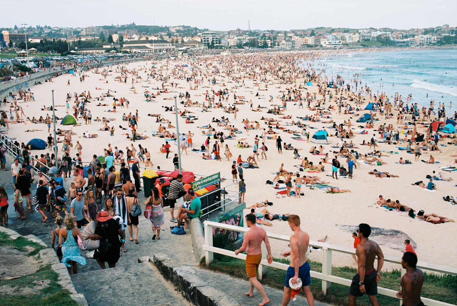 “A photo of New Years day at Bondi Beach, Thousands of people on the beach & in the water. People cue to have a shower in a long line. People are wearing bathers, it’s a hot day in Sydney Australia”.  Artwork Prints, wall art,  travel Australia, Photographic prints,  Framed artwor,k Beach, Photography Photography for sale Film photography Vintage photo style,  Interior design, Film photography, film photography, Bondi beach Sydney, Street photography prints,