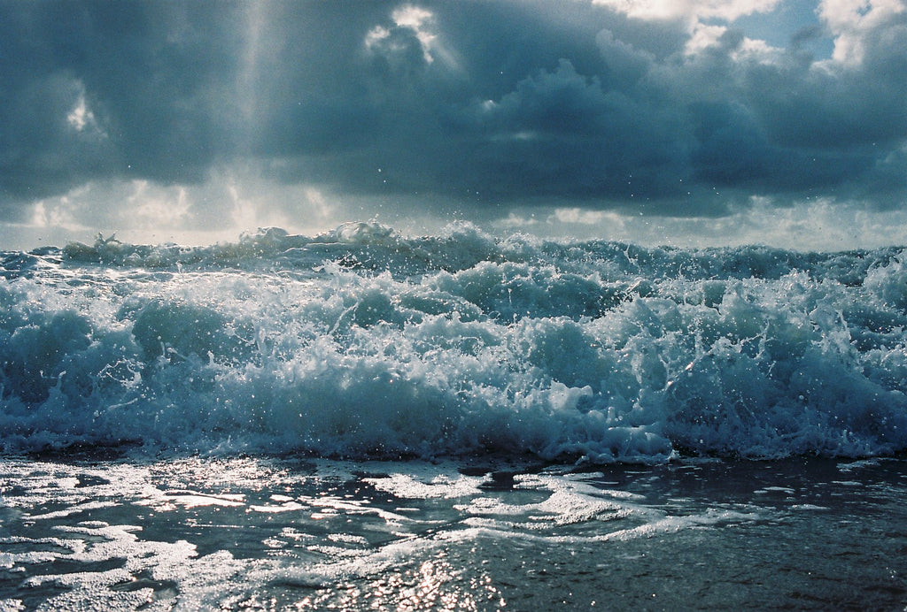 A photography waves breaking in Byron bay.  the water is blue with large white & blue clouds.