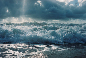 A photography waves breaking in Byron bay.  the water is blue with large white & blue clouds.