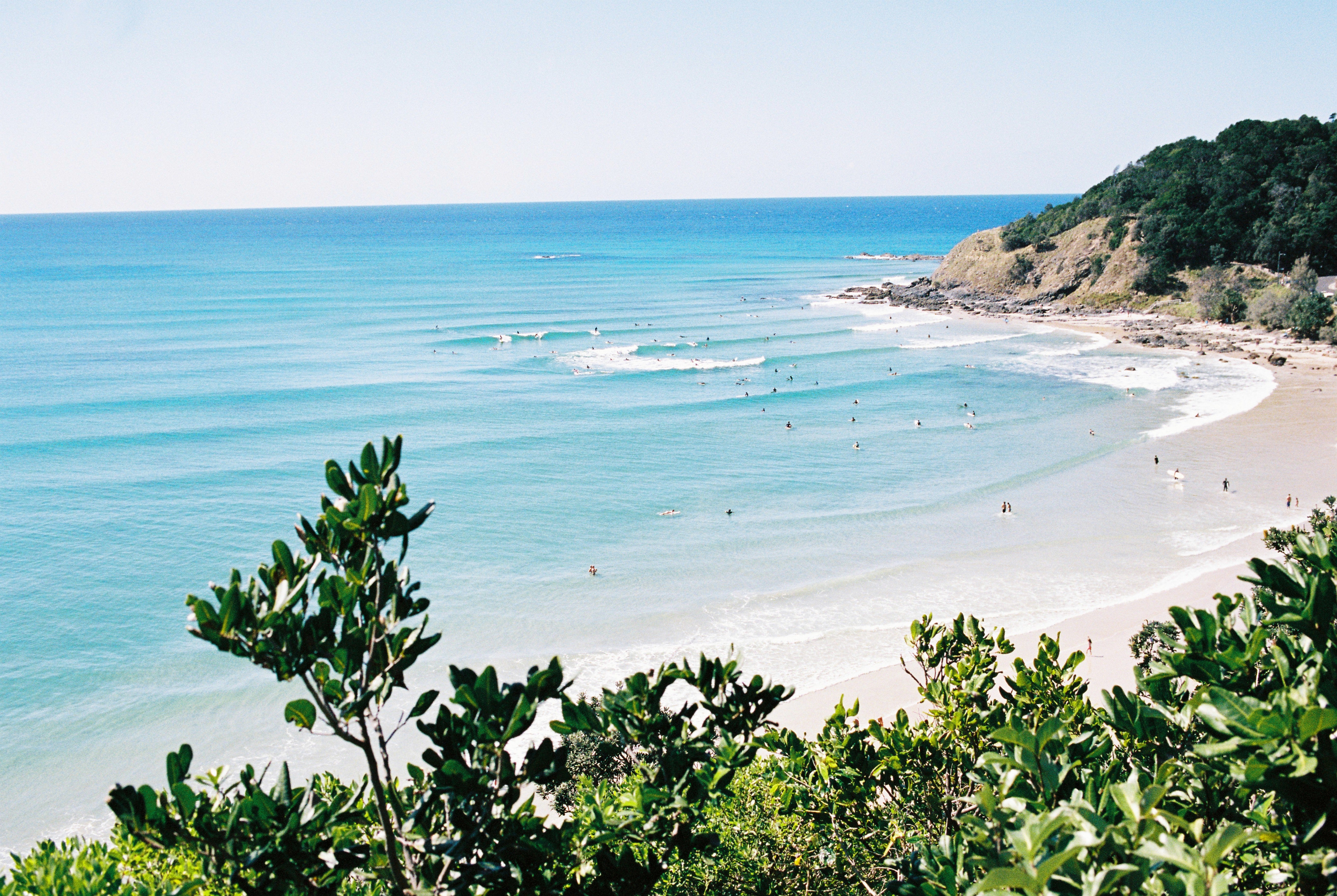 A photography of Wategos beach photographed from the hill. in Byron bay. People surfing in & the water is blue.