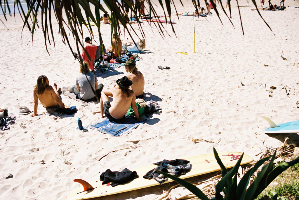 A group of hip young mens relax on the beach at Wategos beach in Byron bay.