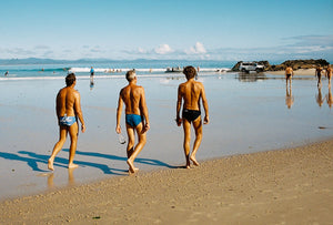 Three local men in speedos walk along Byron Bay's clarkes beach ready to go for a swim