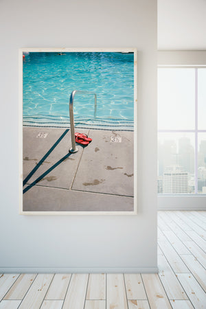 A photo gallery with a framed photograph on th wall. A photograph of a swimming pool with red flip flops on the edge of the pool. There is a marker in the concrete that says three & a half feet. The photograph is taken at the Ace Hotel on Palm Springs.