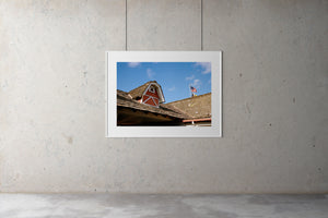 A vintage motel with shingle roof tiles & farmhouse barn roof features. There is an American flag on the roof. There are blue skies. Film photography, Vintage photo style,  Interior design, buy art, photography art, buy art, Prints for sale, art prints, colour photography, vintage photo style, American flag, California, pioneer, 