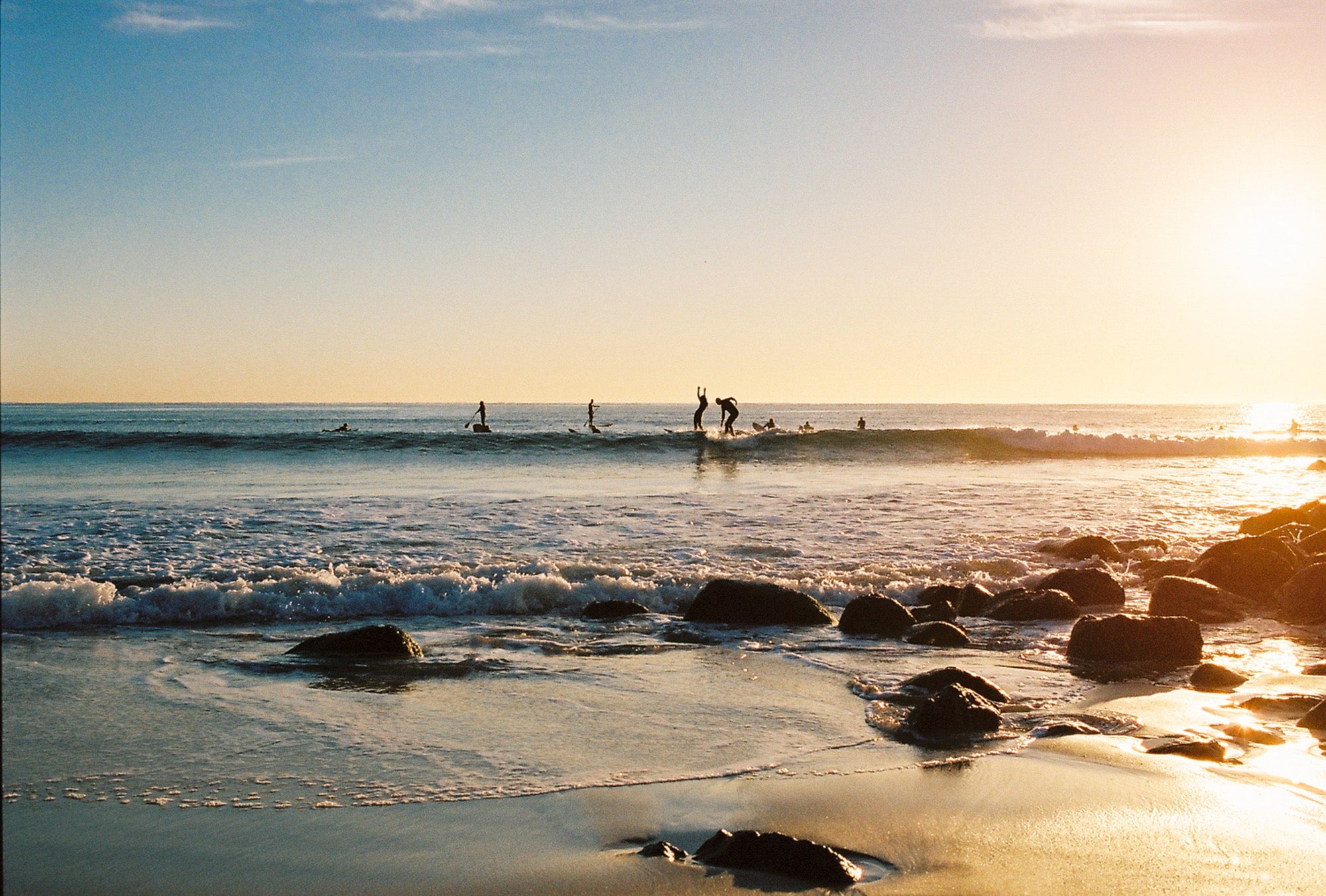 locals surf at sunset in Byron bay. purple skies & blue water with rocks on the beach