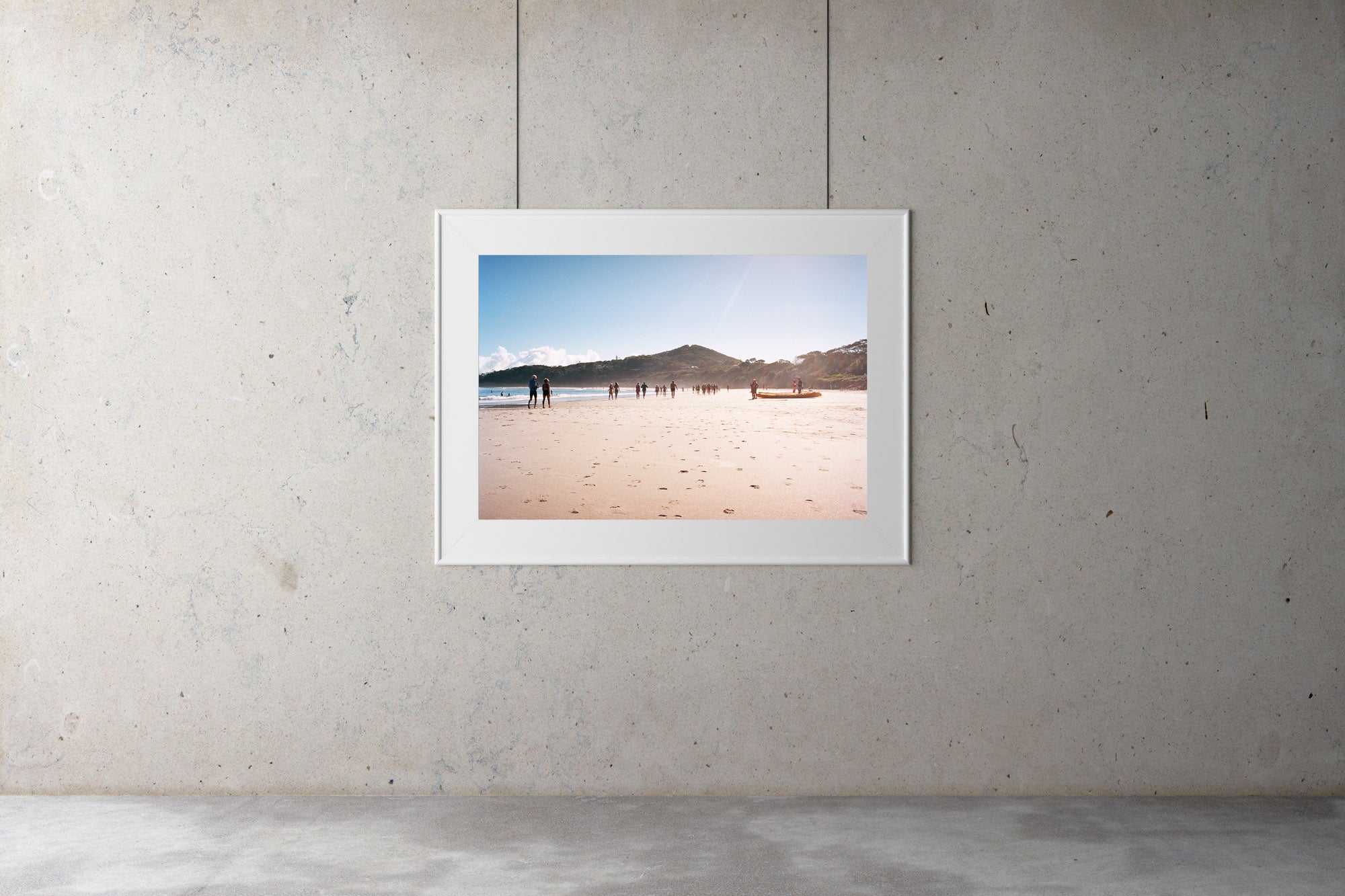 A photography galley with a print on the wall, Byron bay beach with people walking in the distance, blue calm water, blue sky. Two men on a kayak head to the water, Artwork Prints, wall art, Melbourne travel,  Photographic prints,  Framed artwork,  Australian  Photography, wall art, beach prints, coastal prints, ocean prints,  Film photography, Vintage photo, style  Interior design, Pictures Abstract film photography, photography art, Australia, sun, beach, Byron bay,