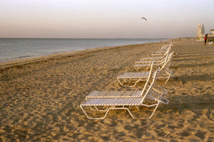 Empty Miami Beach in the morning, there are white sun lounges in the yellow sand & blue calm waters