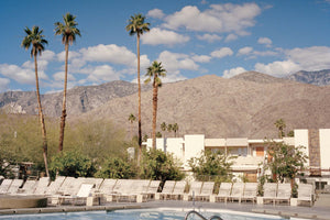 A photograph of a swimming pool looking out on palm trees & large mountains. Blue skies, clouds & Palm trees. USA,