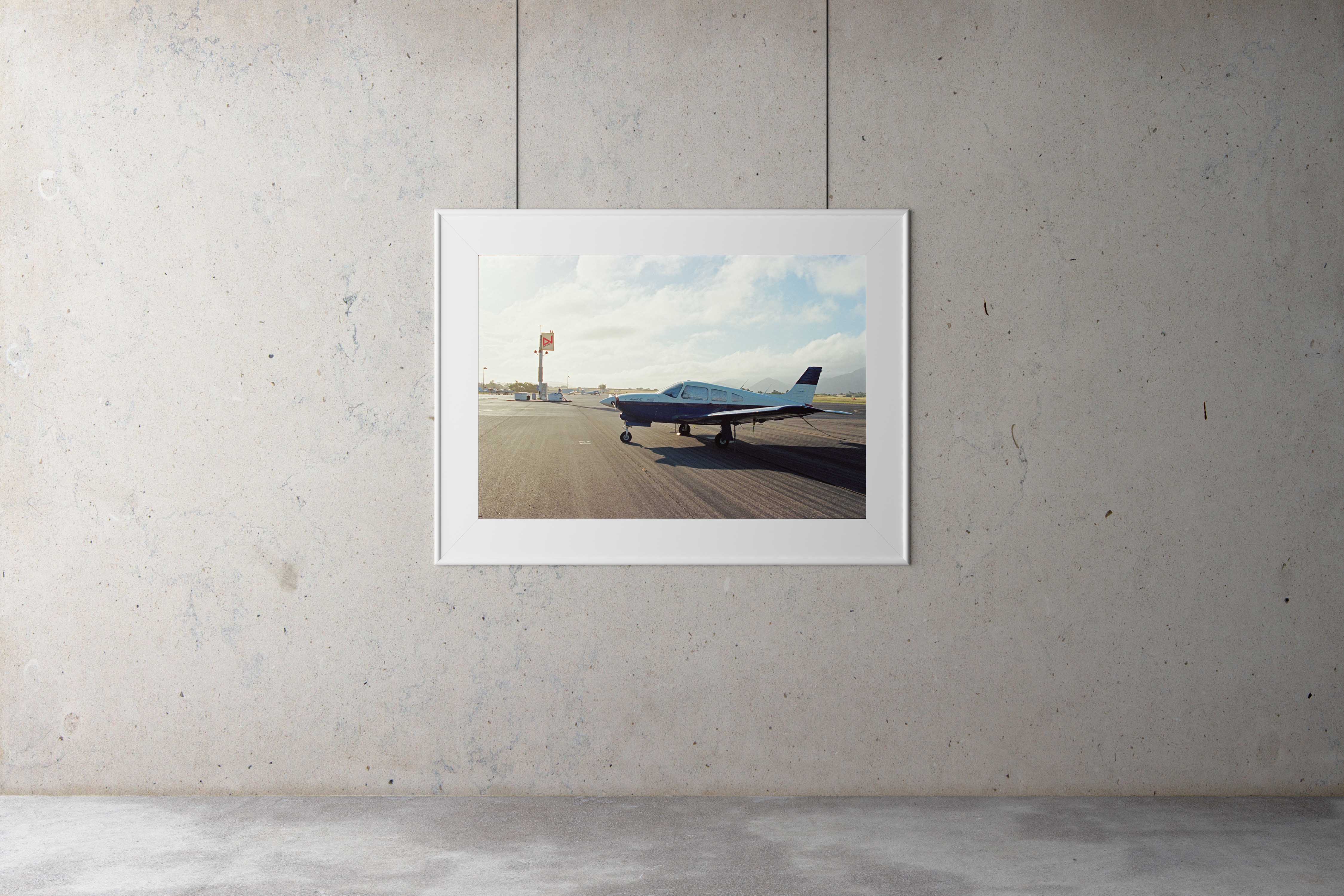 A photographic gallery framed picture of a 1970's single engine plane on a lonely tarmac in California