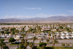 A photograph taken from a high vantage point of a large caravan park with mountains & desert in the background.