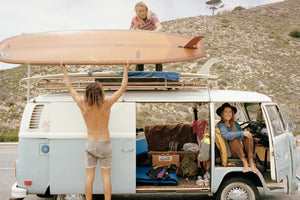 A Photo of two surfers putting their vintage longboards on the roof of an old Kombi van.  A young girl inside the Kombi smiling at the camera.  artwork, Prints, wall art, photographic prints,      prints, ocean, framed artwork, photography, film photography, vintage photo style,  Interior design, beach, buy art, photography art, buy art, Prints for sale, art prints, colour photography, sun, beach, sun baking, retro, interior design artwork, surfing, Kombi van, Malibu
