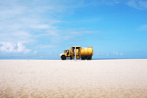 A yellow truck on a beach in California, the sky is blue & the sand is yellow.