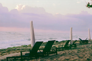 Miami beach with black sun lounges & white umbrella's, purple skies & clouds, sand & blue calm water.