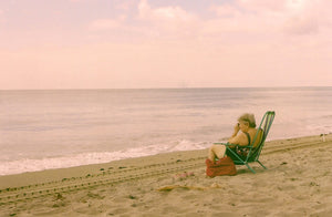 Miami Beach in the morning, an old lady sits on ther beach taking a photo of the ocean, sand & blue calm water.